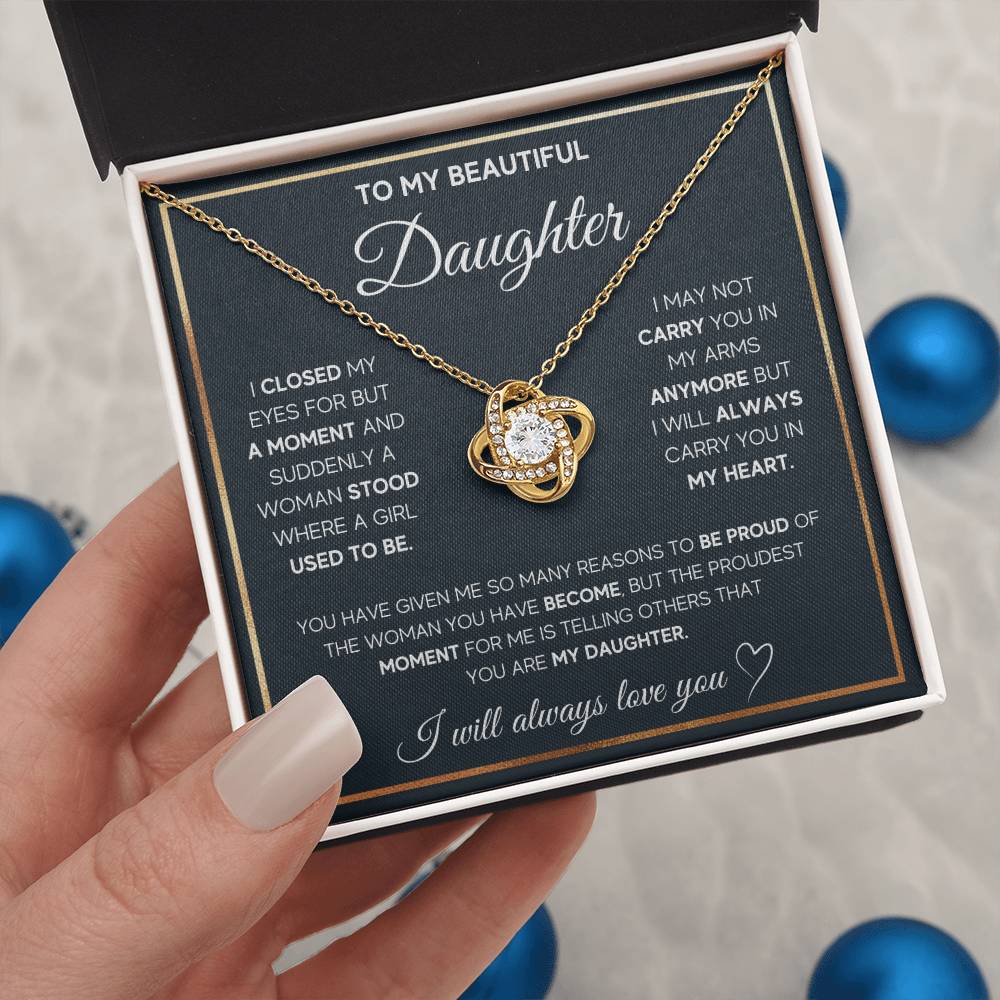 a hand holding  a gold knot-shaped pendant in a box with a heartfelt message, on a decorative background