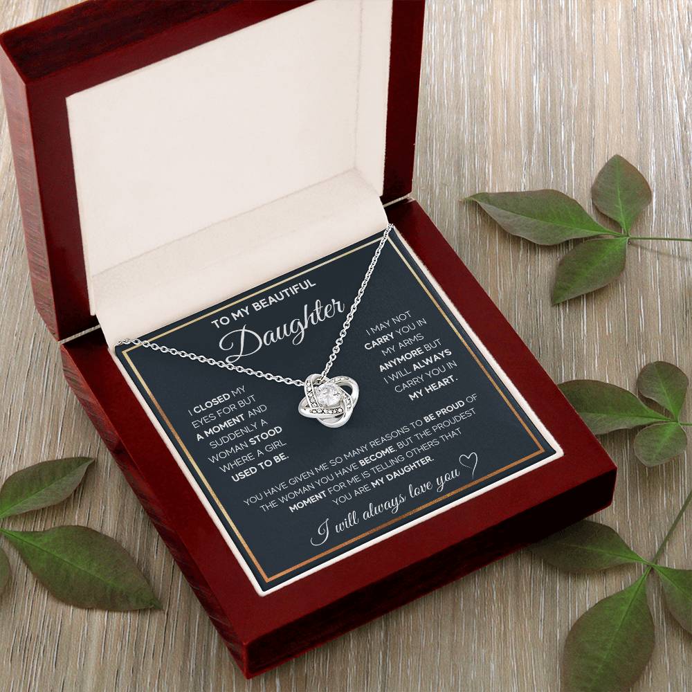 A silver necklace with a knot-shaped pendant in a luxury box, a gift from a parent to their daughter with a heartfelt message. in a leaf background